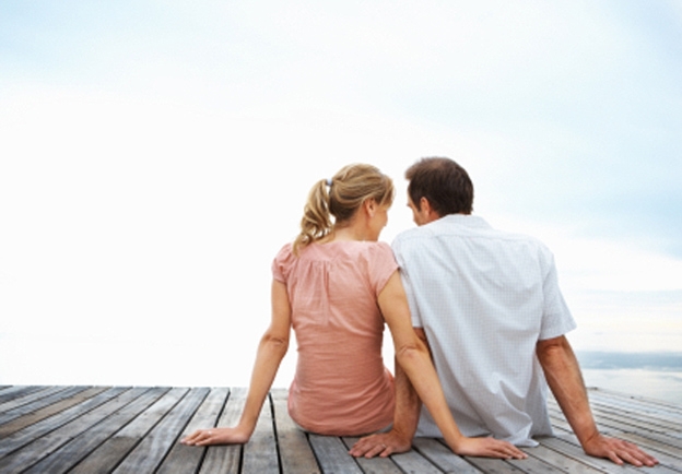 A romantic couple sitting on a jetty with the sky as the background